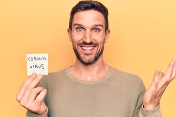 Young handsome man holding reminder with coronavirus message over yellow background celebrating achievement with happy smile and winner expression with raised hand