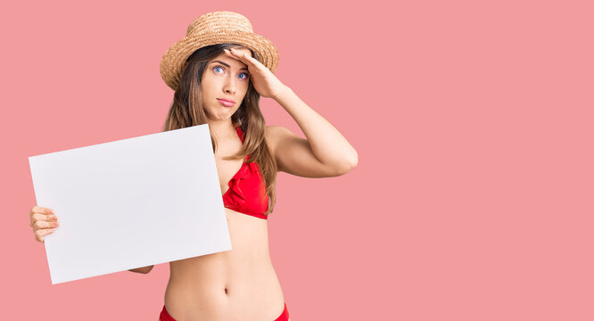 Beautiful caucasian young woman wearing bikini holding blank empty banner stressed and frustrated with hand on head, surprised and angry face