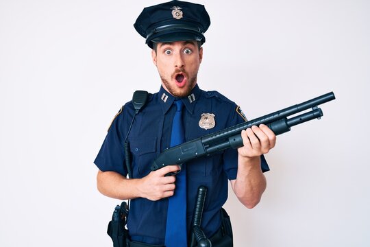 Young caucasian man wearing police uniform holding shotgun afraid and shocked with surprise and amazed expression, fear and excited face.