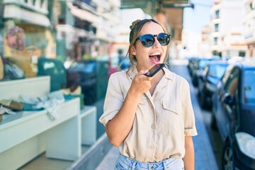 Young beautiful blonde caucasian woman smiling happy outdoors on a sunny day using smartphone