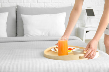 Obraz na płótnie Canvas Chambermaid putting tasty breakfast on bed in hotel room