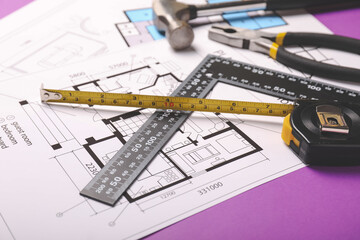 Measuring tape with builder's supplies and blueprints on color background
