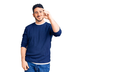 Young hispanic man wearing casual clothes smiling and confident gesturing with hand doing small size sign with fingers looking and the camera. measure concept.