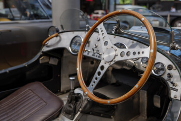 Selected focus at unique decorated shiny and wooden steering wheel and metallic dashboard inside vintage classic old sport car. 