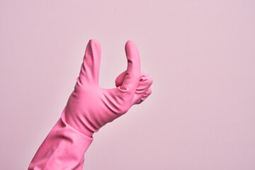 Hand of caucasian young man with cleaning glove over isolated pink background picking and taking invisible thing, holding object with fingers showing space