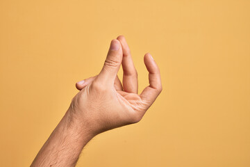Hand of caucasian young man showing fingers over isolated yellow background snapping fingers for success, easy and click symbol gesture with hand