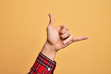 Hand of caucasian young man showing fingers over isolated yellow background gesturing Hawaiian...