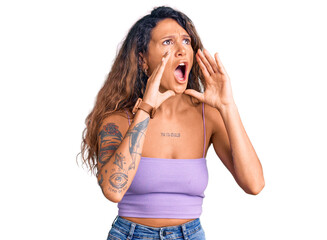 Young hispanic woman with tattoo wearing casual clothes shouting angry out loud with hands over mouth