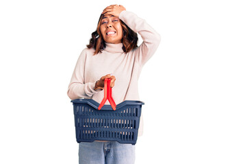 Fototapeta na wymiar Young beautiful mixed race woman holding supermarket shopping basket stressed and frustrated with hand on head, surprised and angry face