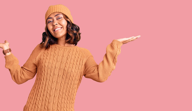 Young beautiful mixed race woman wearing wool sweater and winter hat clueless and confused expression with arms and hands raised. doubt concept.