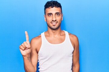 Young hispanic man wearing casual clothes smiling with an idea or question pointing finger up with...