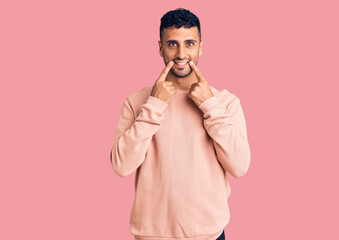 Fototapeta premium Young hispanic man wearing casual clothes smiling with open mouth, fingers pointing and forcing cheerful smile