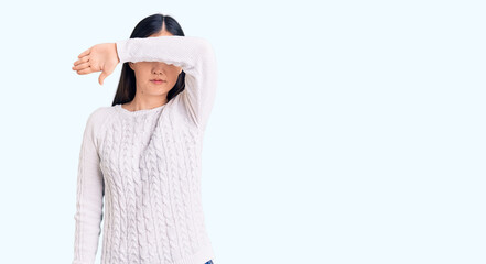 Young beautiful chinese woman wearing casual sweater covering eyes with arm, looking serious and sad. sightless, hiding and rejection concept