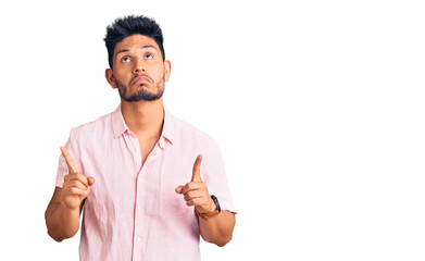 Handsome latin american young man wearing casual summer shirt pointing up looking sad and upset, indicating direction with fingers, unhappy and depressed.