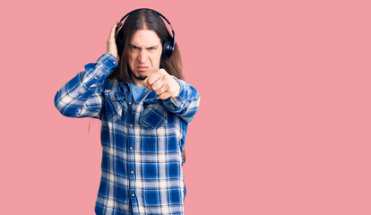 Young adult man with long hair listening to music using headphones annoyed and frustrated shouting with anger, yelling crazy with anger and hand raised