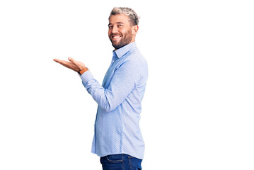 Young handsome blond man wearing elegant shirt pointing aside with hands open palms showing copy space, presenting advertisement smiling excited happy