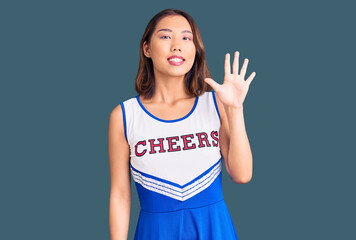 Young beautiful chinese girl wearing cheerleader uniform showing and pointing up with fingers...