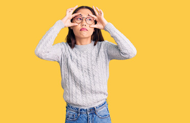 Young beautiful chinese girl wearing casual clothes trying to open eyes with fingers, sleepy and...