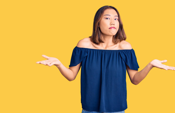 Young beautiful chinese girl wearing casual clothes clueless and confused expression with arms and hands raised. doubt concept.