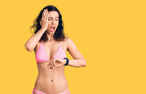 Young beautiful hispanic woman wearing bikini looking at the watch time worried, afraid of getting late