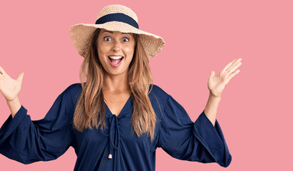 Middle age hispanic woman wearing summer hat celebrating crazy and amazed for success with arms raised and open eyes screaming excited. winner concept