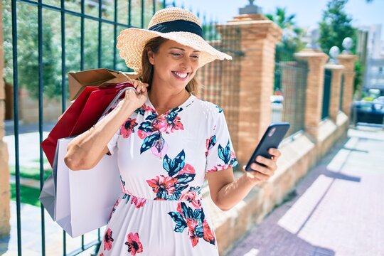 Middle age woman holding shopping bags and using smartphone at the city