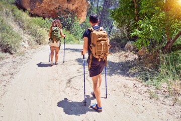 Beautiful couple of hiker on back view wearing backpack doing trekking using hiking stick at forest - obrazy, fototapety, plakaty