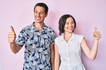 Beautiful couple wearing casual clothes looking proud, smiling doing thumbs up gesture to the side