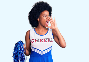 Young african american woman wearing cheerleader uniform holding pompom shouting and screaming loud...