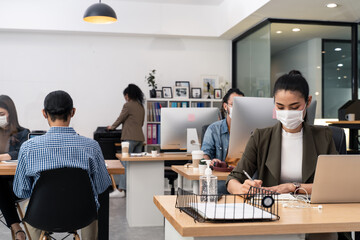 Asian young businesswoman wearing mask working on computer in office.