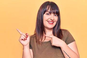 Young plus size woman wearing casual clothes smiling and looking at the camera pointing with two hands and fingers to the side.