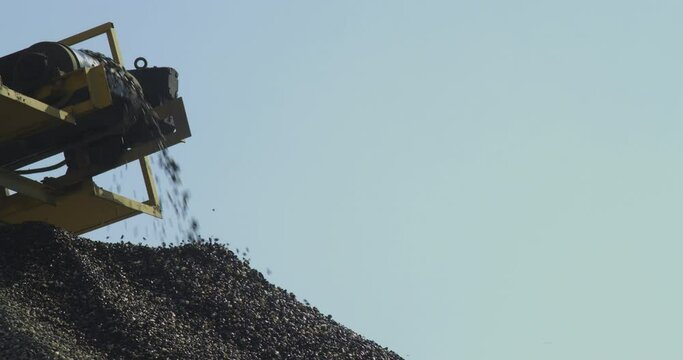 Crushing plant machine in the work process, transportation, and separation of gravel rocks on the conveyor belt, line production, the blue sky in the background, close-up shot.