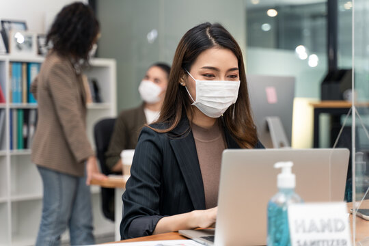 Asian young businesswoman wearing mask working on computer in office. - Powered by Adobe