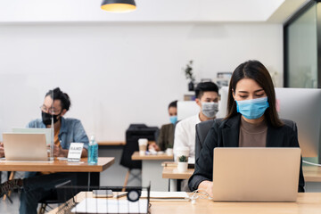 Asian young businesswoman wearing mask working on computer in office.