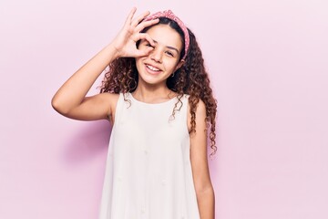 Fototapeta premium Beautiful kid girl with curly hair wearing casual clothes smiling happy doing ok sign with hand on eye looking through fingers