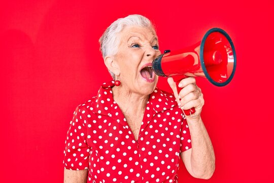 Senior beautiful grey-haired woman screaming using megaphone over isolated red background