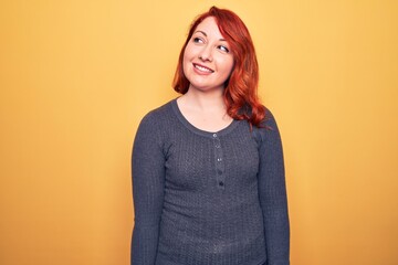 Obraz premium Young beautiful redhead woman wearing casual sweater standing over yellow background looking to side, relax profile pose with natural face and confident smile.