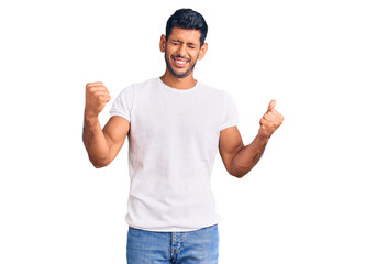 Naklejka premium Young latin man wearing casual clothes very happy and excited doing winner gesture with arms raised, smiling and screaming for success. celebration concept.