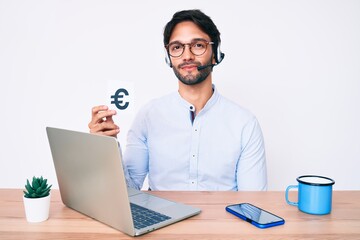 Handsome hispanic man working at the office holding euro banner thinking attitude and sober expression looking self confident