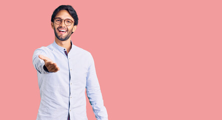 Fototapeta premium Handsome hispanic man wearing business shirt and glasses smiling friendly offering handshake as greeting and welcoming. successful business.