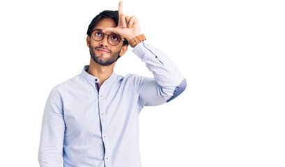 Handsome hispanic man wearing business shirt and glasses making fun of people with fingers on forehead doing loser gesture mocking and insulting.