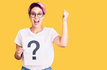 Young beautiful woman with pink hair holding question mark screaming proud, celebrating victory and success very excited with raised arms