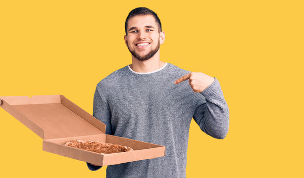 Young handsome man holding delivery italian pizza pointing finger to one self smiling happy and proud