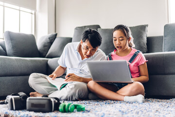 Father and asian kid little girl learning and looking at laptop computer making homework studying knowledge with online education e-learning system.children video conference with teacher tutor at home