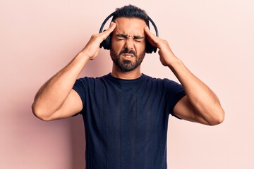 Young hispanic man listening to music using headphones suffering from headache desperate and stressed because pain and migraine. hands on head.