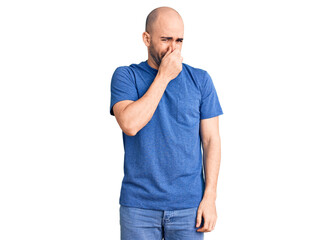 Young handsome man wearing casual t shirt smelling something stinky and disgusting, intolerable smell, holding breath with fingers on nose. bad smell