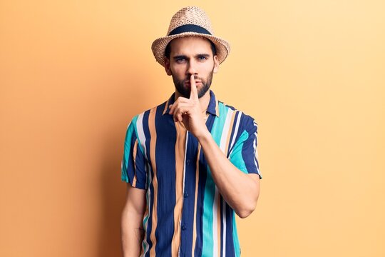 Young handsome man with beard wearing summer hat and shirt asking to be quiet with finger on lips. silence and secret concept.