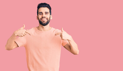 Young handsome man with beard wearing casual t-shirt looking confident with smile on face, pointing oneself with fingers proud and happy.