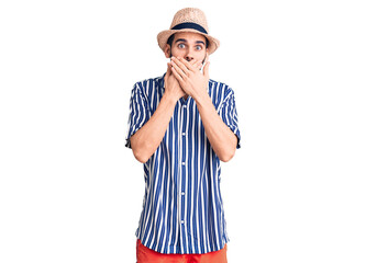 Young handsome man with beard wearing summer hat and striped shirt shocked covering mouth with hands for mistake. secret concept.