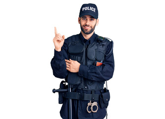 Young handsome man with beard wearing police uniform with a big smile on face, pointing with hand and finger to the side looking at the camera.